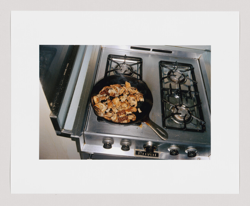 Cast-iron skillet of mushrooms and browned meat cooking on a stainless steel gas stove.