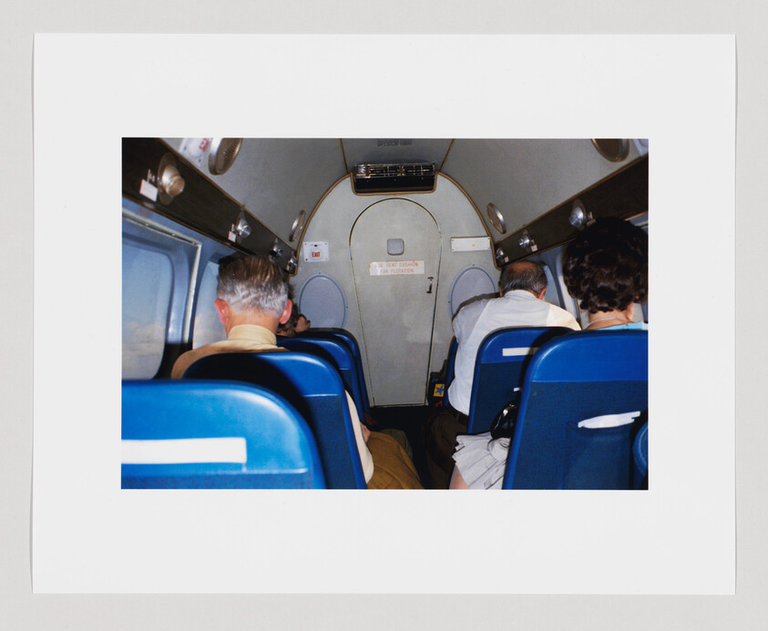 Four people sit in blue seats on a small airplane, facing the closed door at the front.