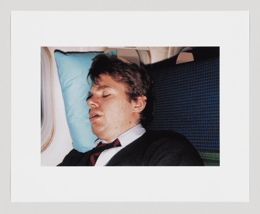 A man sleeping against a blue pillow in an airplane window seat.
