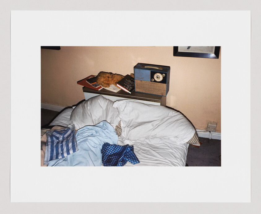 Unmade bed with rumpled pillows, a polka-dot tie and vintage radio on the bedside table.