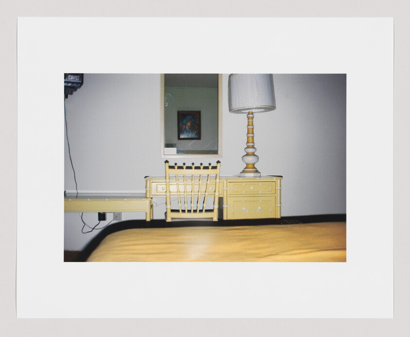 Yellow desk and matching chair with tall lamp beside a bed and mirror on the wall.