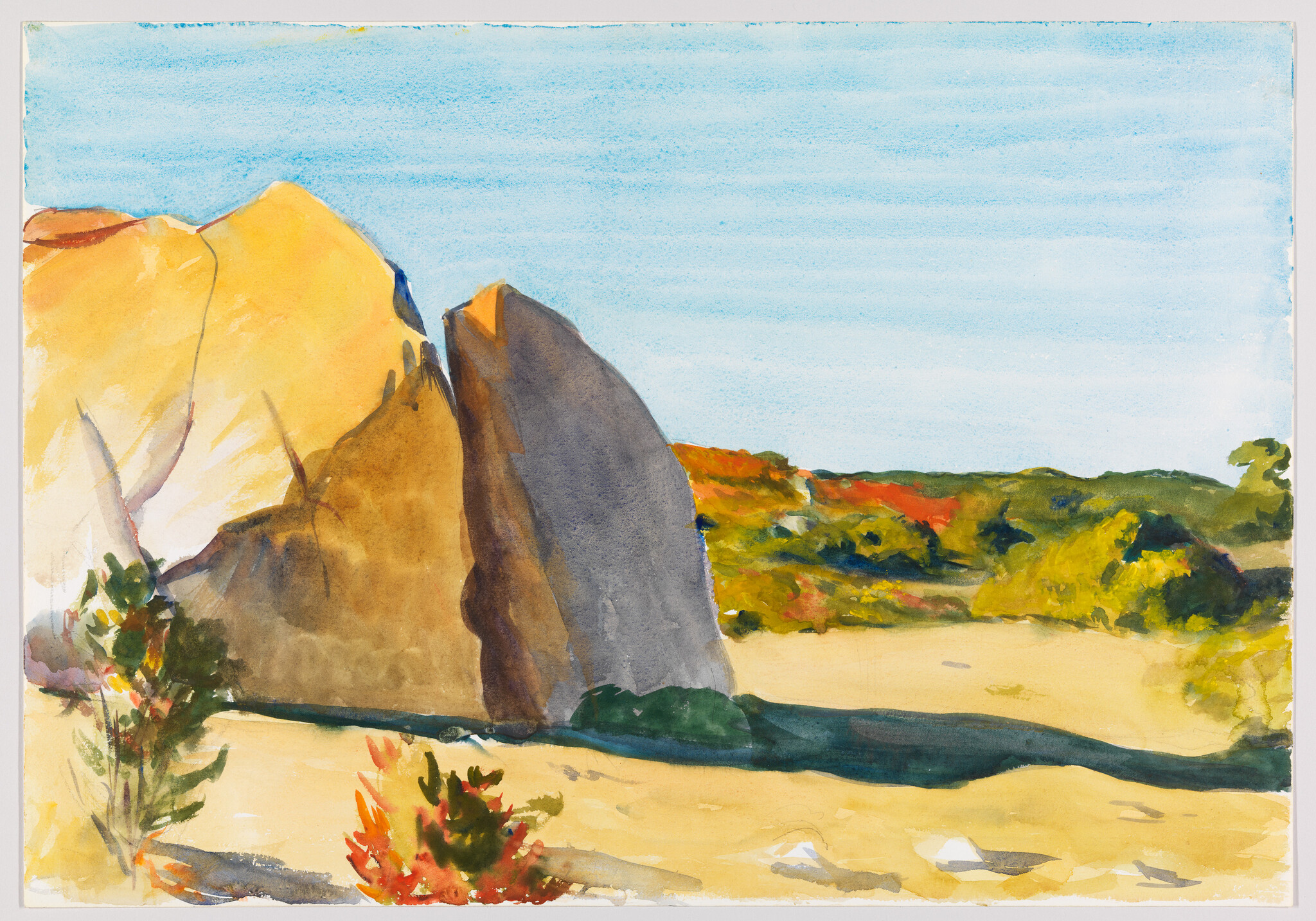 Large sunlit boulders cast a deep shadow across sandy ground and sparse shrubs.