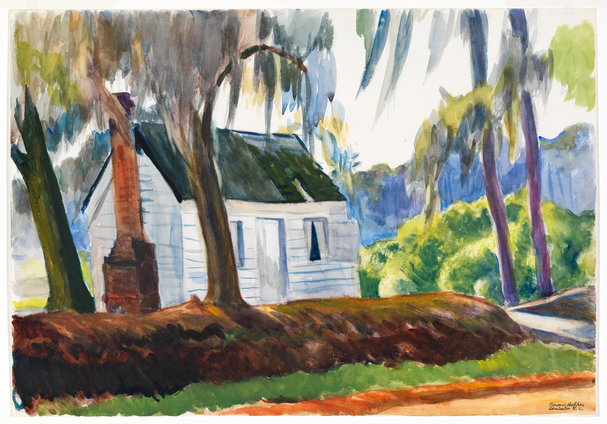 Small white cottage sits shaded among tall trees with sunlit green bushes nearby.