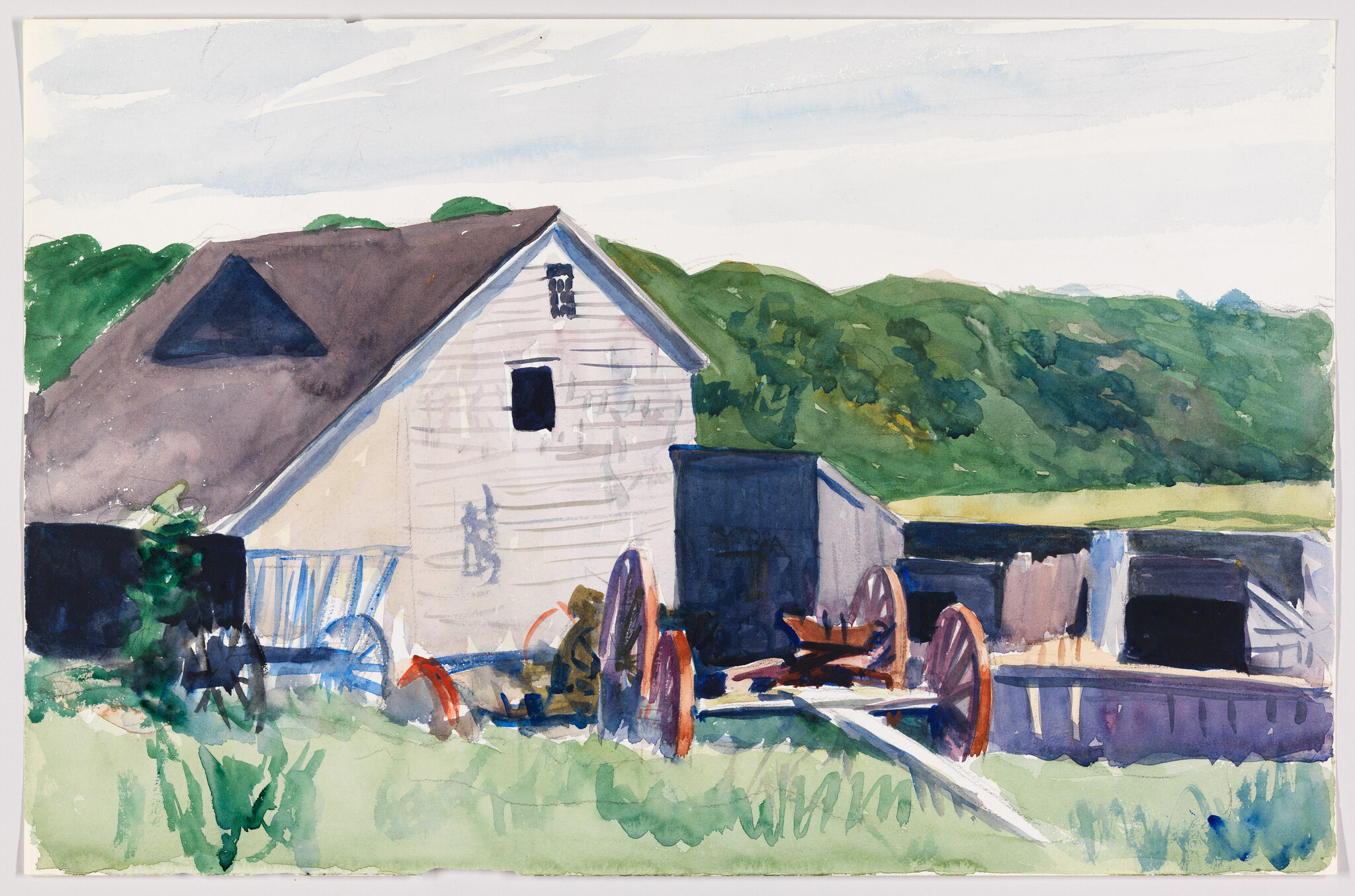 A white barn beside old wooden wagon wheels and green hills under a pale sky.