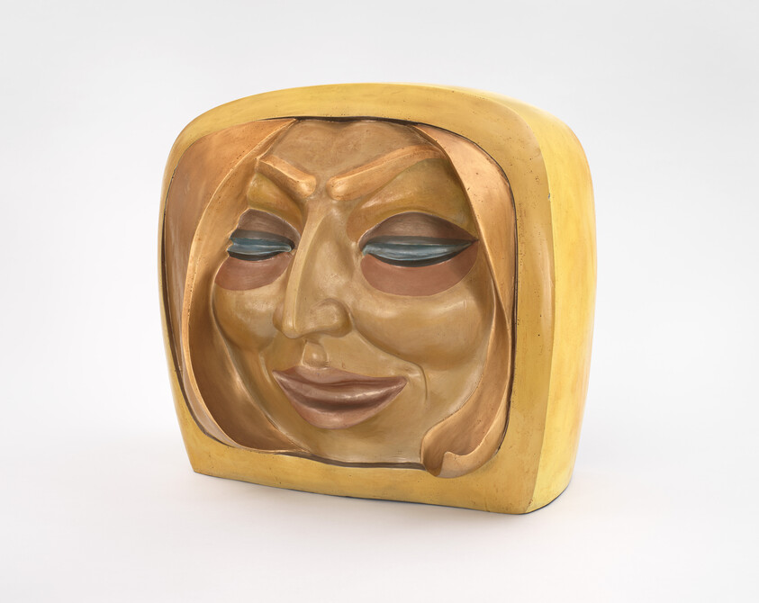 Carved wooden mask with a smiling, hooded face painted in warm yellow and brown tones.
