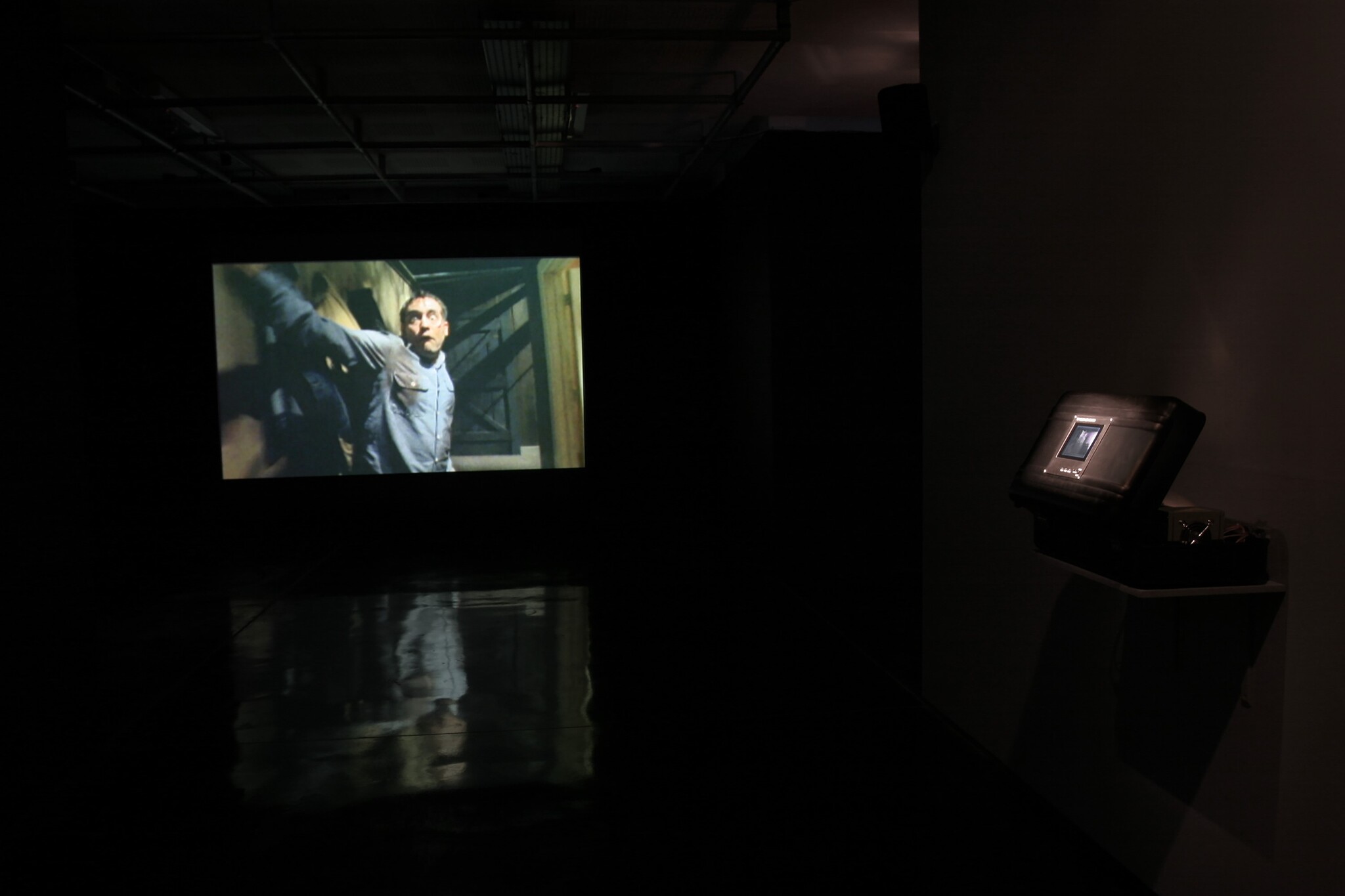 A man in a blue shirt is projected on a screen in a dark room.