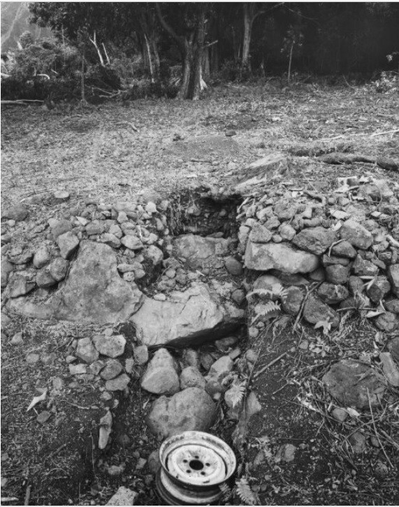 A collapsed dry-stone wall with a gap leading down to rocky ground and a discarded wheel rim.