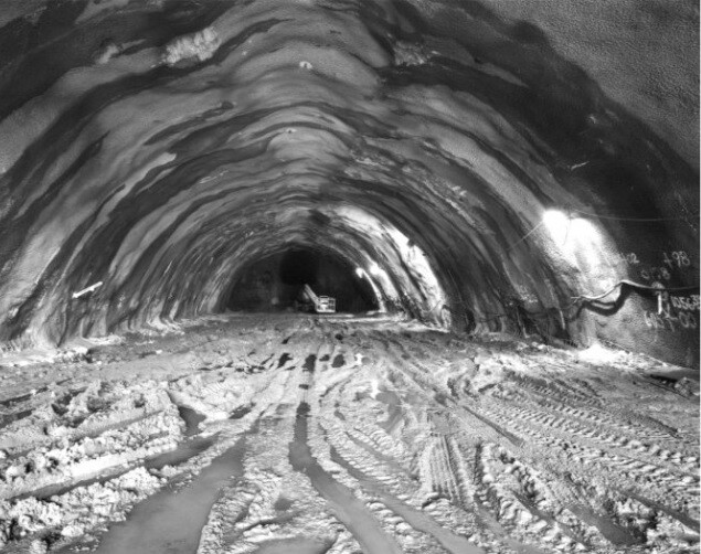 A large, rough tunnel with muddy tracks and a small vehicle in the distance.