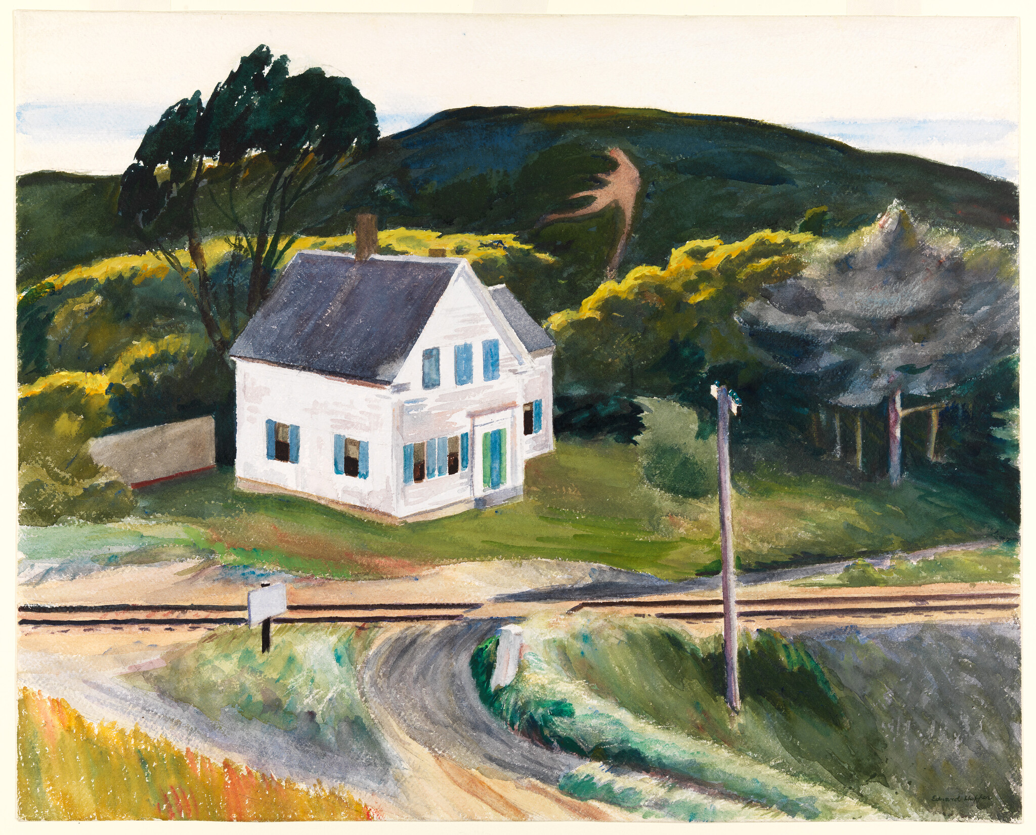 A white farmhouse near railroad tracks with a curved dirt road and tall trees behind.