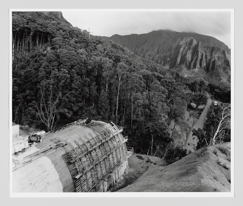 Concrete tunnel under construction on a mountainside with scaffolding and a service truck nearby.