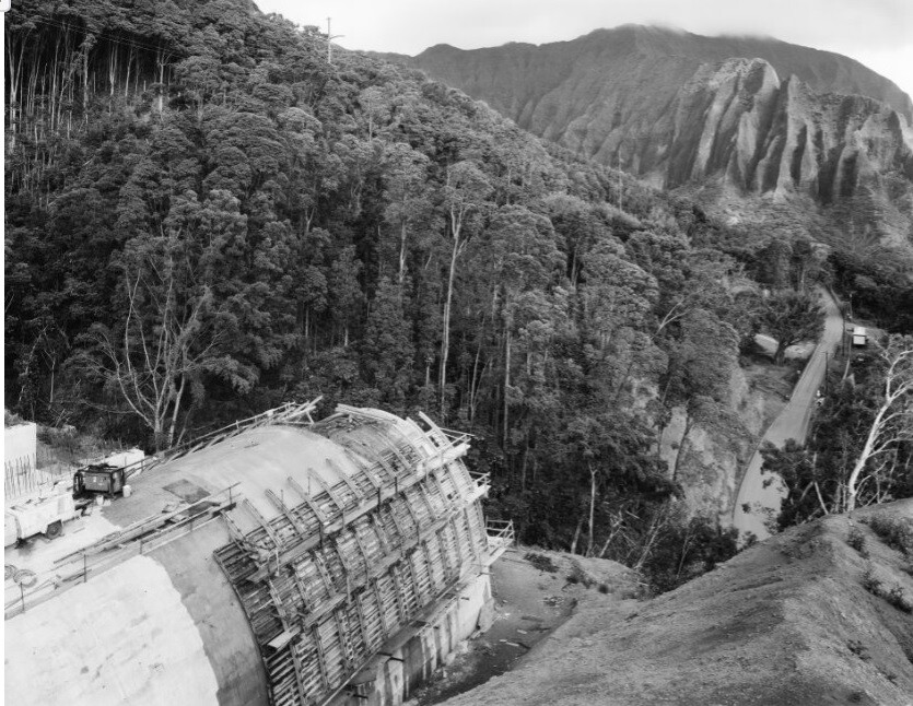 Concrete tunnel under construction on a mountainside with scaffolding and a service truck nearby.