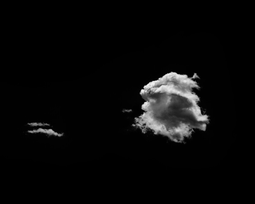 A large white cloud and a small cloud float against a deep black sky.