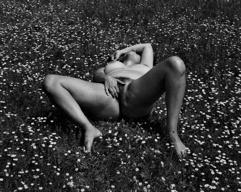 Naked person reclining spread-legged in a field of small white flowers, hand resting on torso.