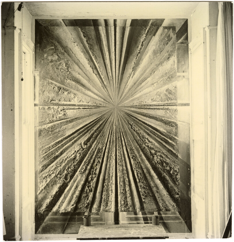 Large radial textured wall panel with starburst pattern installed between two tall windows.