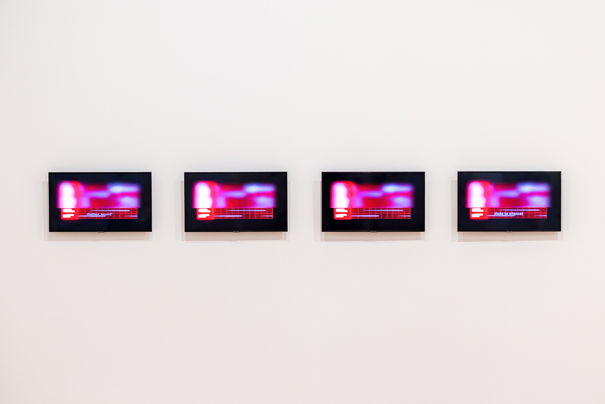 Four wall-mounted screens display blurry red and purple images; one screen shows the words “fades to silence.”