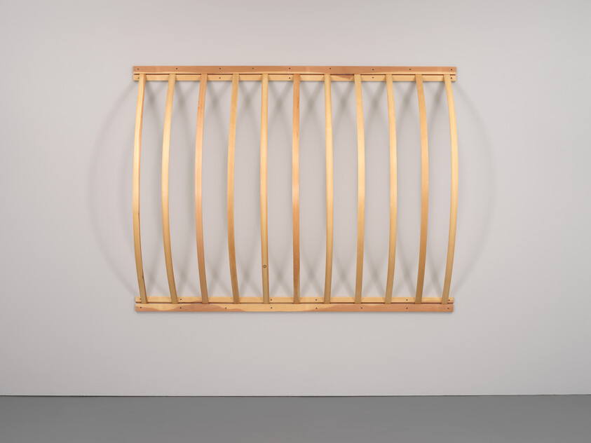 A wooden frame with evenly spaced vertical slats curves outward from a plain white wall.