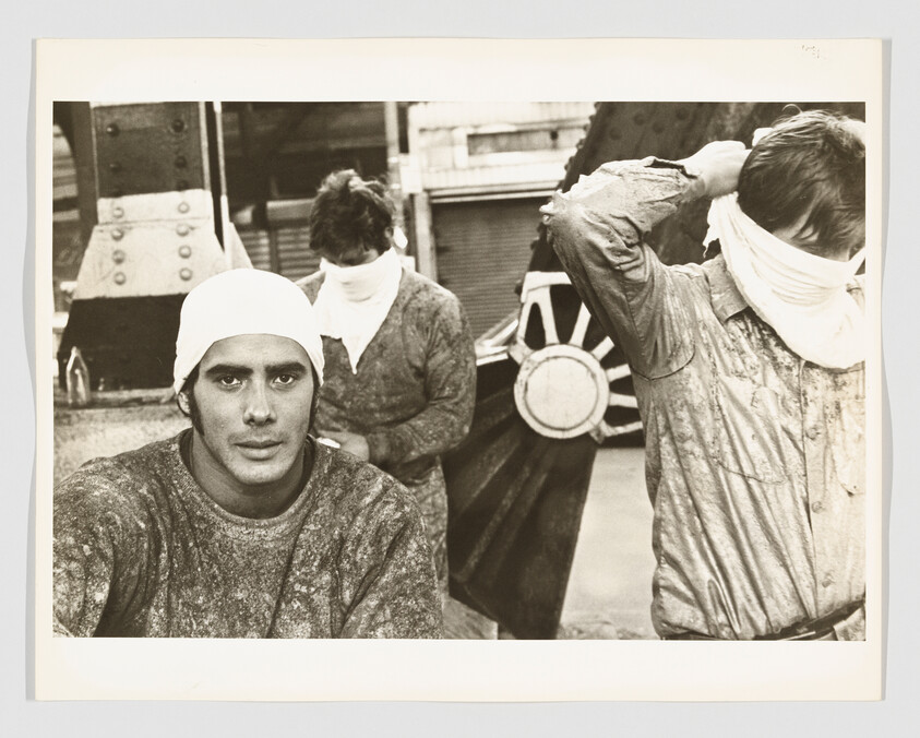 Three factory workers wearing cloth head coverings, one looking at the camera while others adjust cloths.