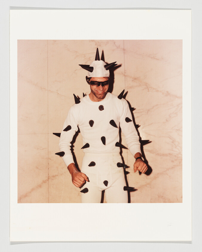 Man wearing white bodysuit covered in black spikes and smiling while posing.