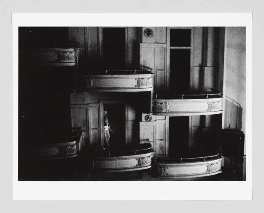 A dimly lit theater balcony with one person standing alone in the shadows near the center.
