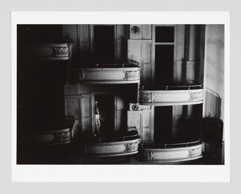 Empty ornate theater boxes with a single figure standing in a dimly lit box.