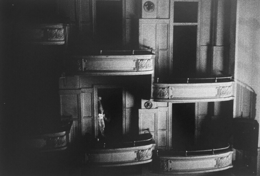 Dimly lit theater balconies with a person standing in one of the doorways.