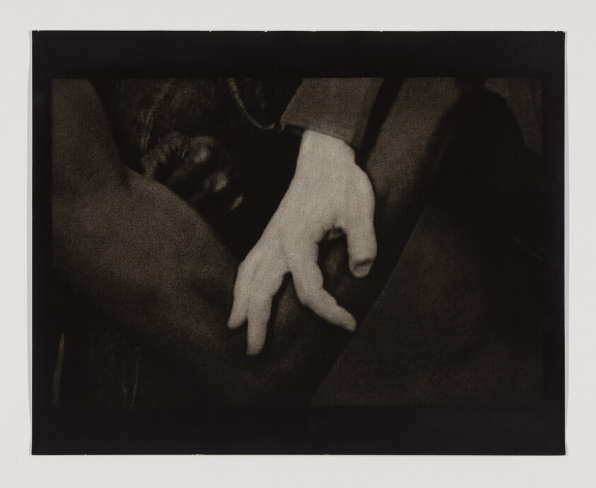 A pale hand gently rests on a dark-skinned person's thigh, fingers relaxed.