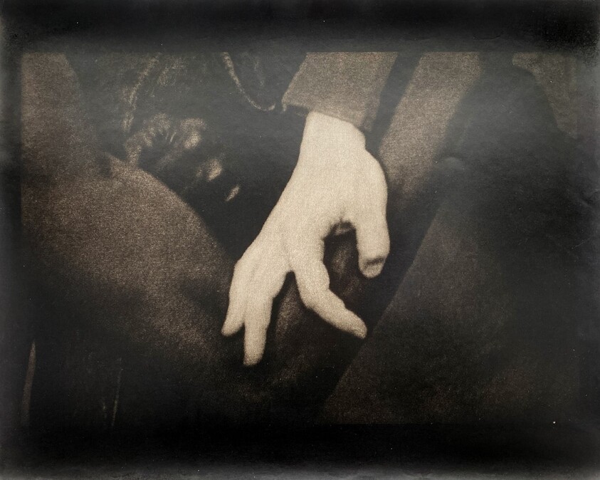 A hand rests gently on a dark fabric, fingers slightly curled.