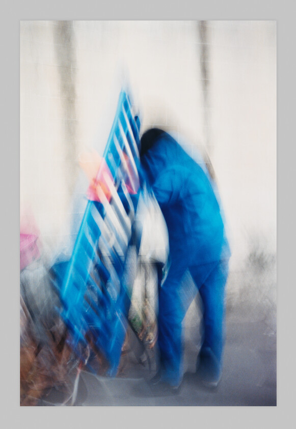 A person in blue clothing stands next to a blue object, both appearing blurry and out of focus.