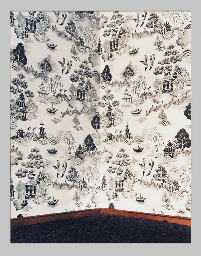 A corner of a room with patterned wallpaper showing trees, birds, boats, and buildings in black and white.