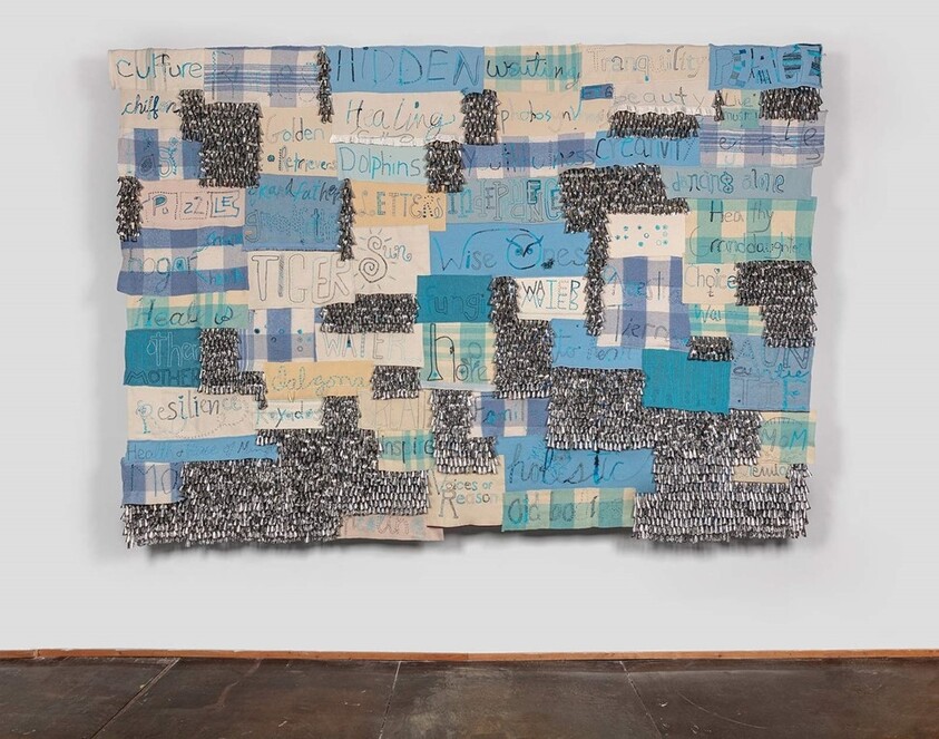A large fabric artwork with blue and beige patches, handwritten words like “TIGER,” “WATER,” and “HIDDEN” visible.