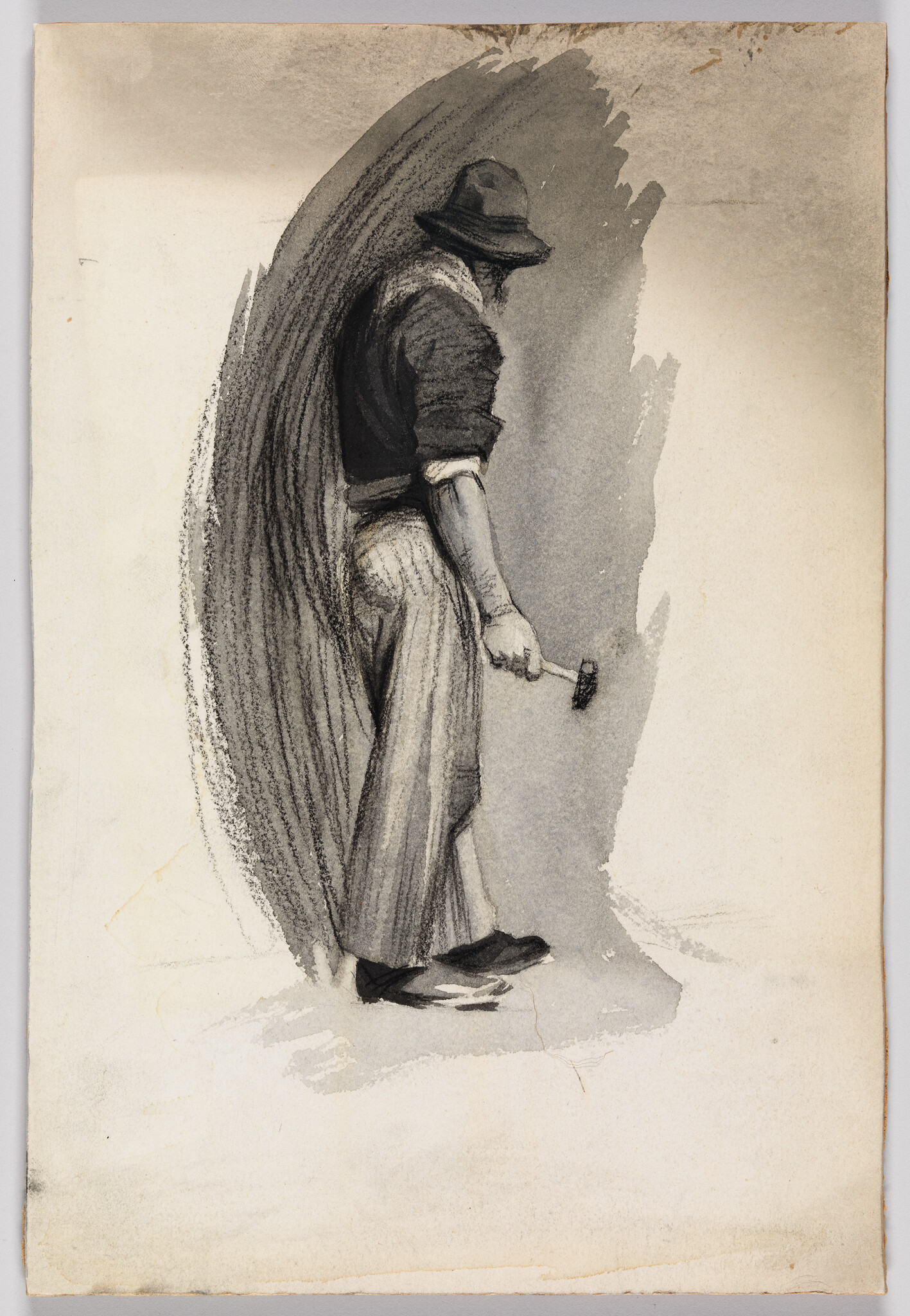 A man wearing a hat and rolled sleeves holds a small hammer while looking down.