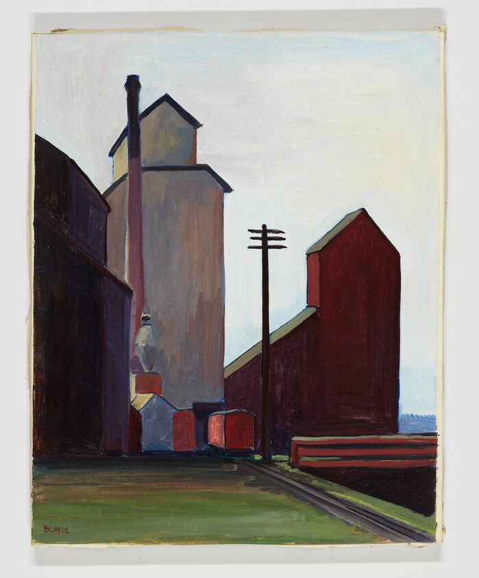 Tall grain elevators and dark industrial buildings beside railroad tracks under a pale sky.