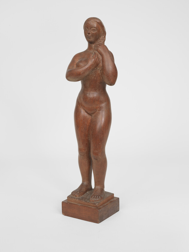 A small wooden sculpture of a standing nude woman with hands raised to her neck on a base.