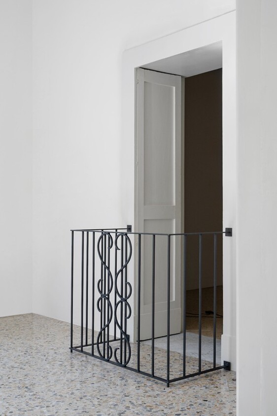 A decorative black metal railing blocks a doorway inside a white room with terrazzo flooring.