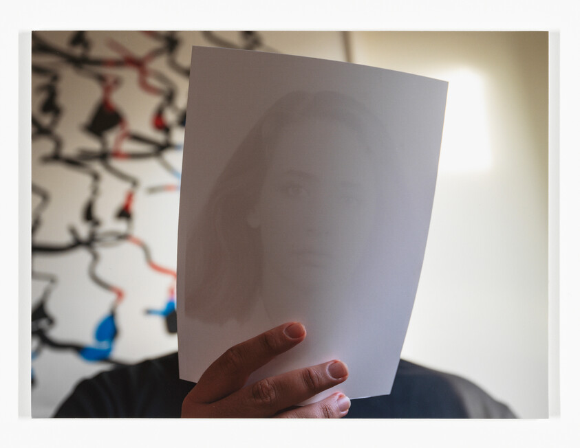 Person holds a sheet of paper with a faint printed face obscuring their own face.