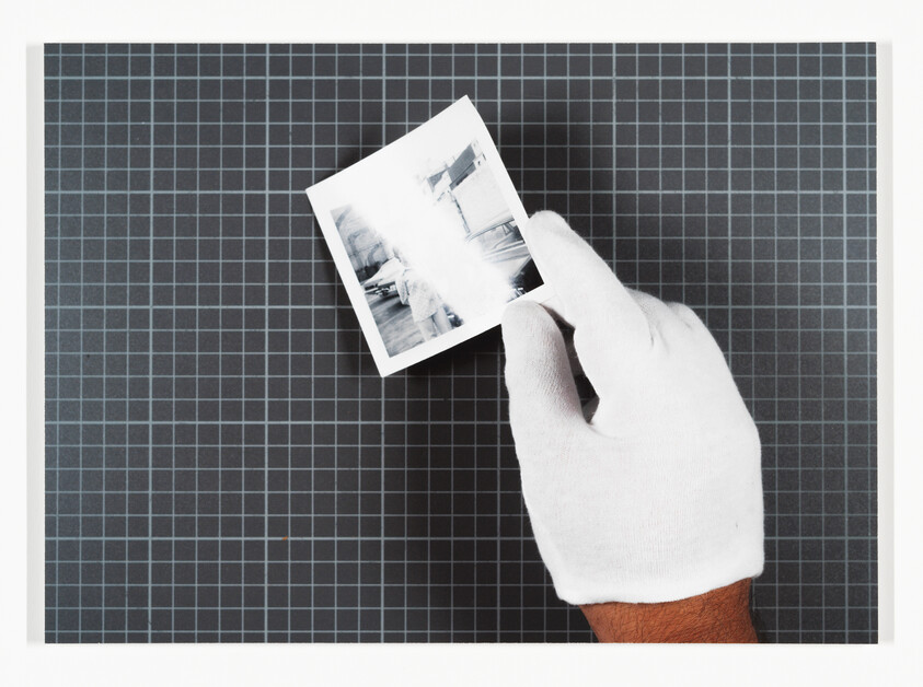 A gloved hand holds a small black-and-white photograph above a grid cutting mat.