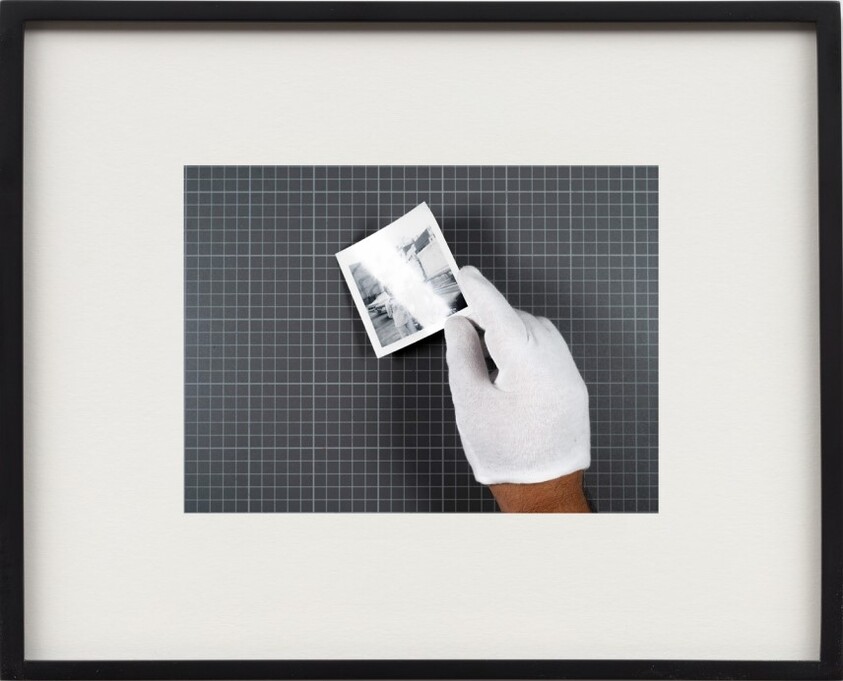 A gloved hand holds a small black-and-white photograph above a grid cutting mat.