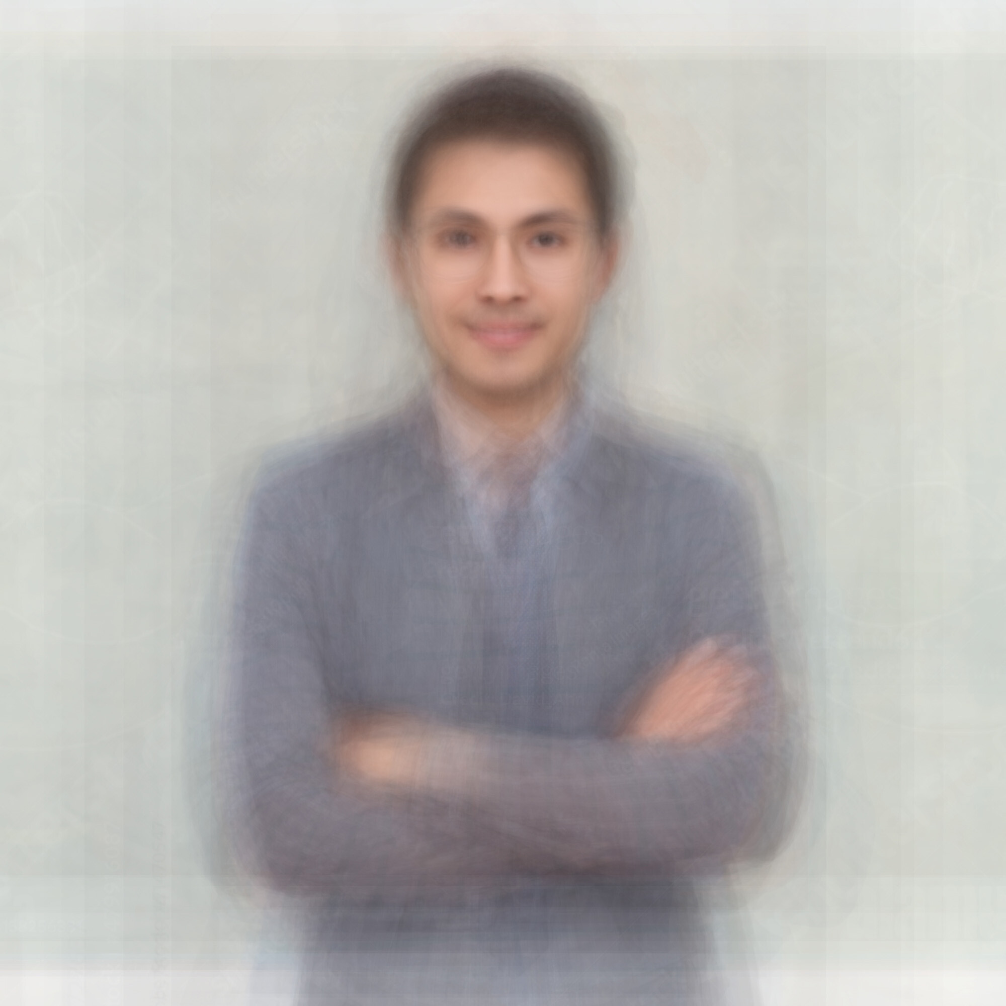 A smiling man in a blazer stands with his arms crossed against a light background.