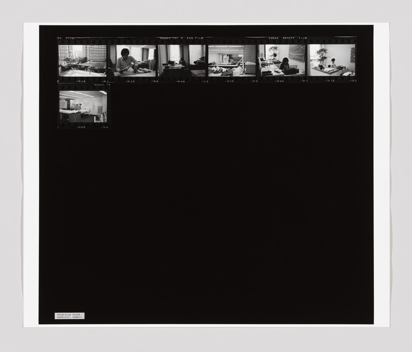 A contact sheet of black-and-white film negatives showing small office scenes along the top edge.