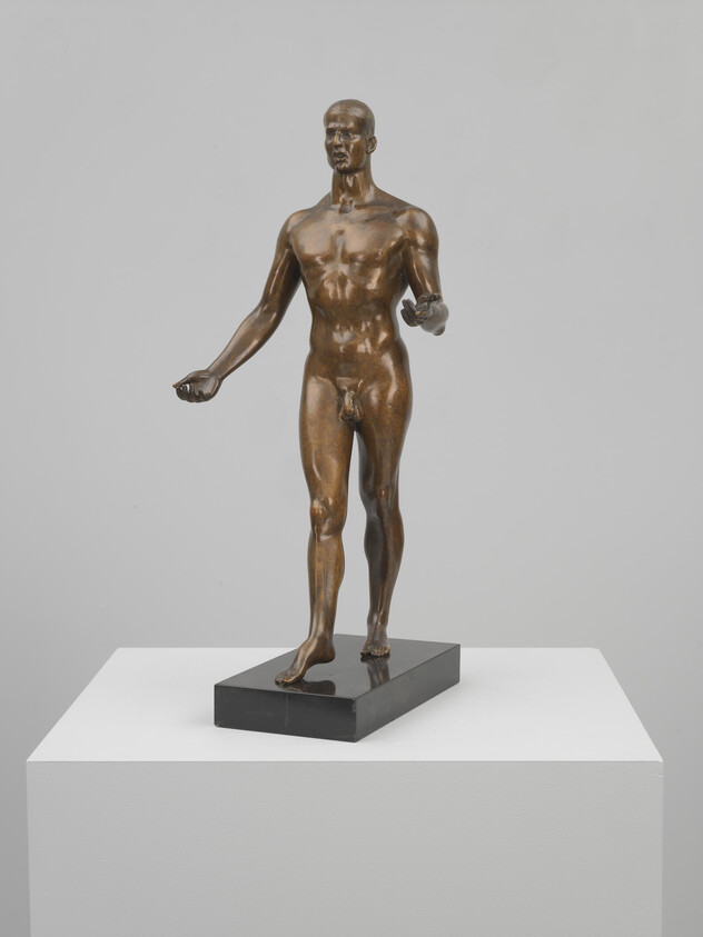 Bronze life-size nude male statue standing with arms slightly extended on a black rectangular base.