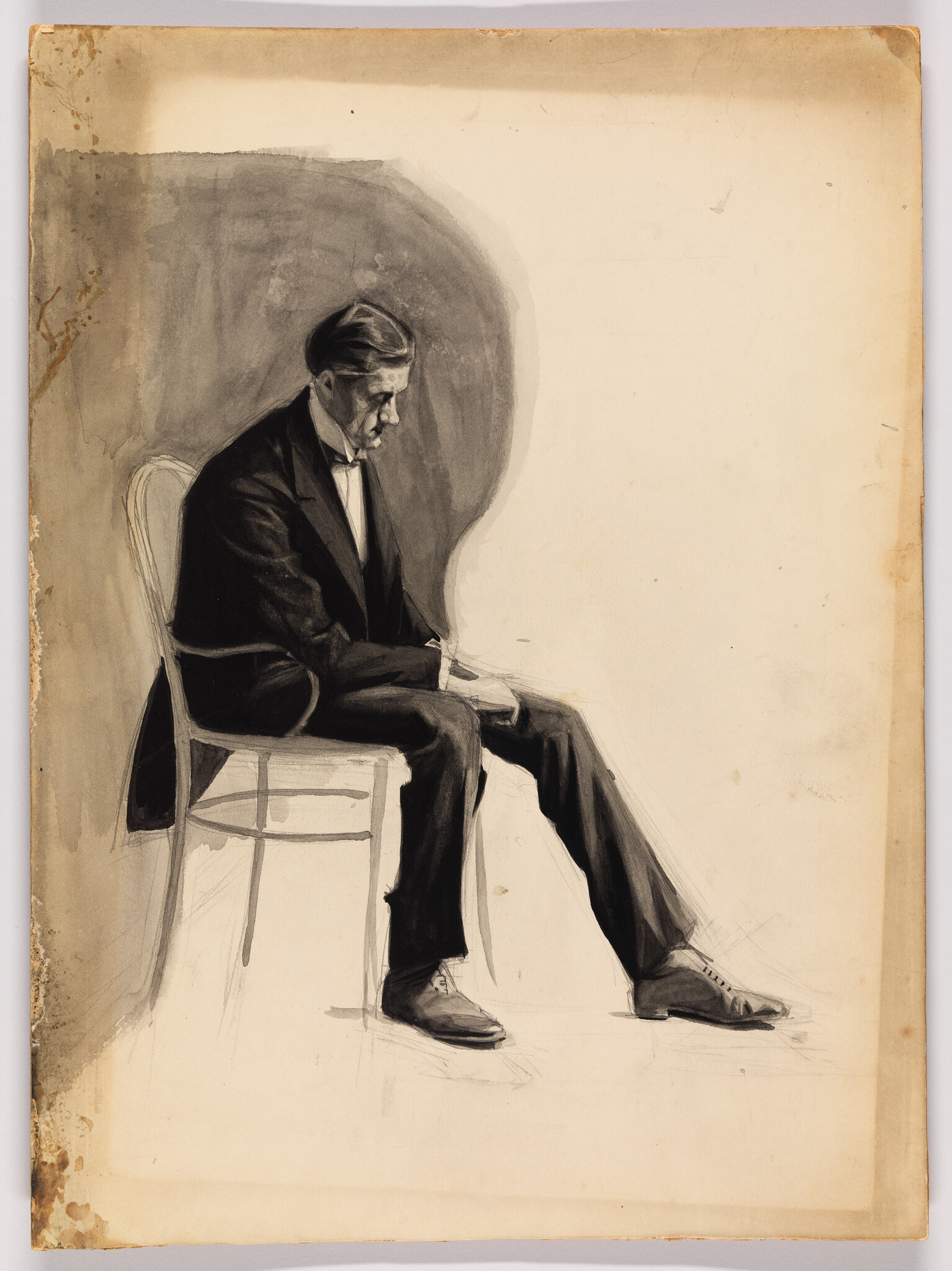 A man in a suit sits on a chair looking down with hands in his lap.