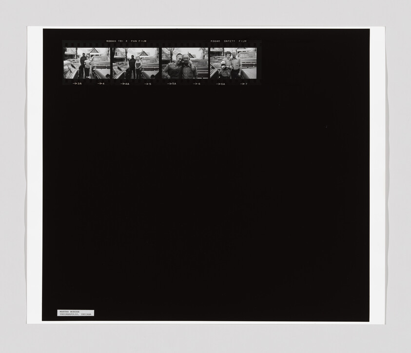Five small black-and-white film frames show people standing and posing near a car in a residential area.