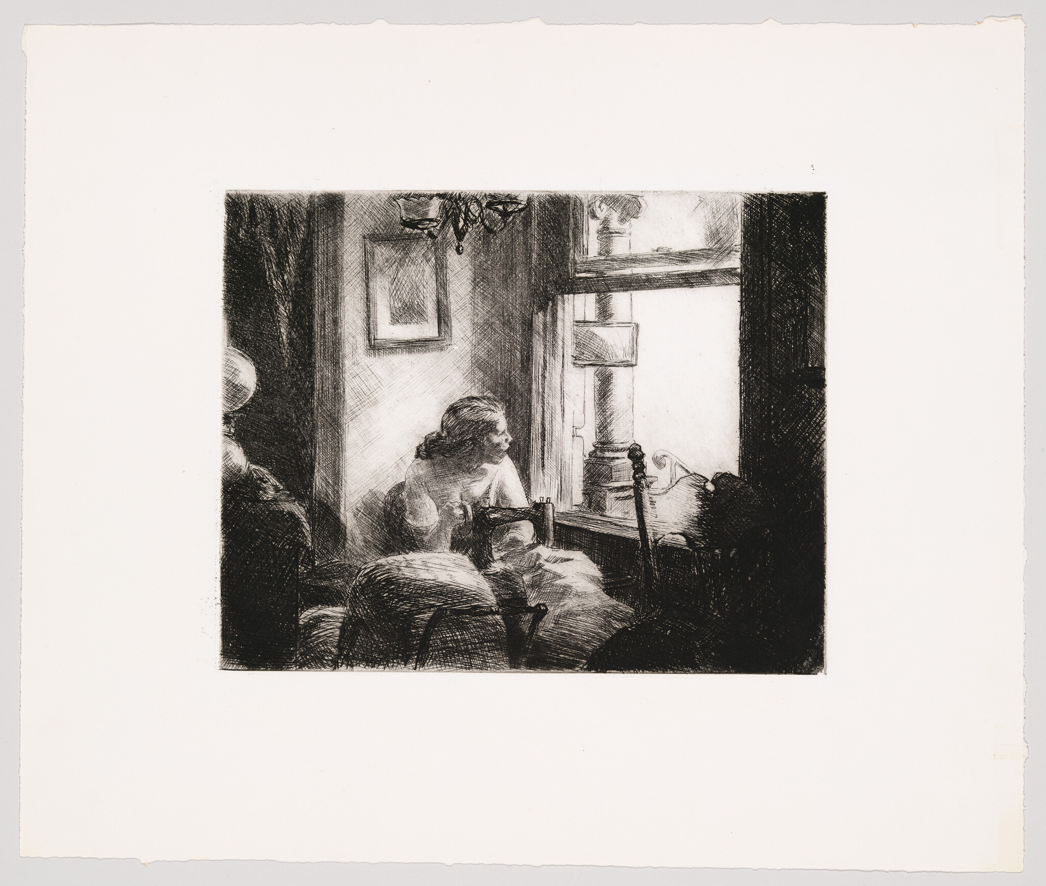 A woman sits by a window sewing while looking thoughtfully out onto the street.