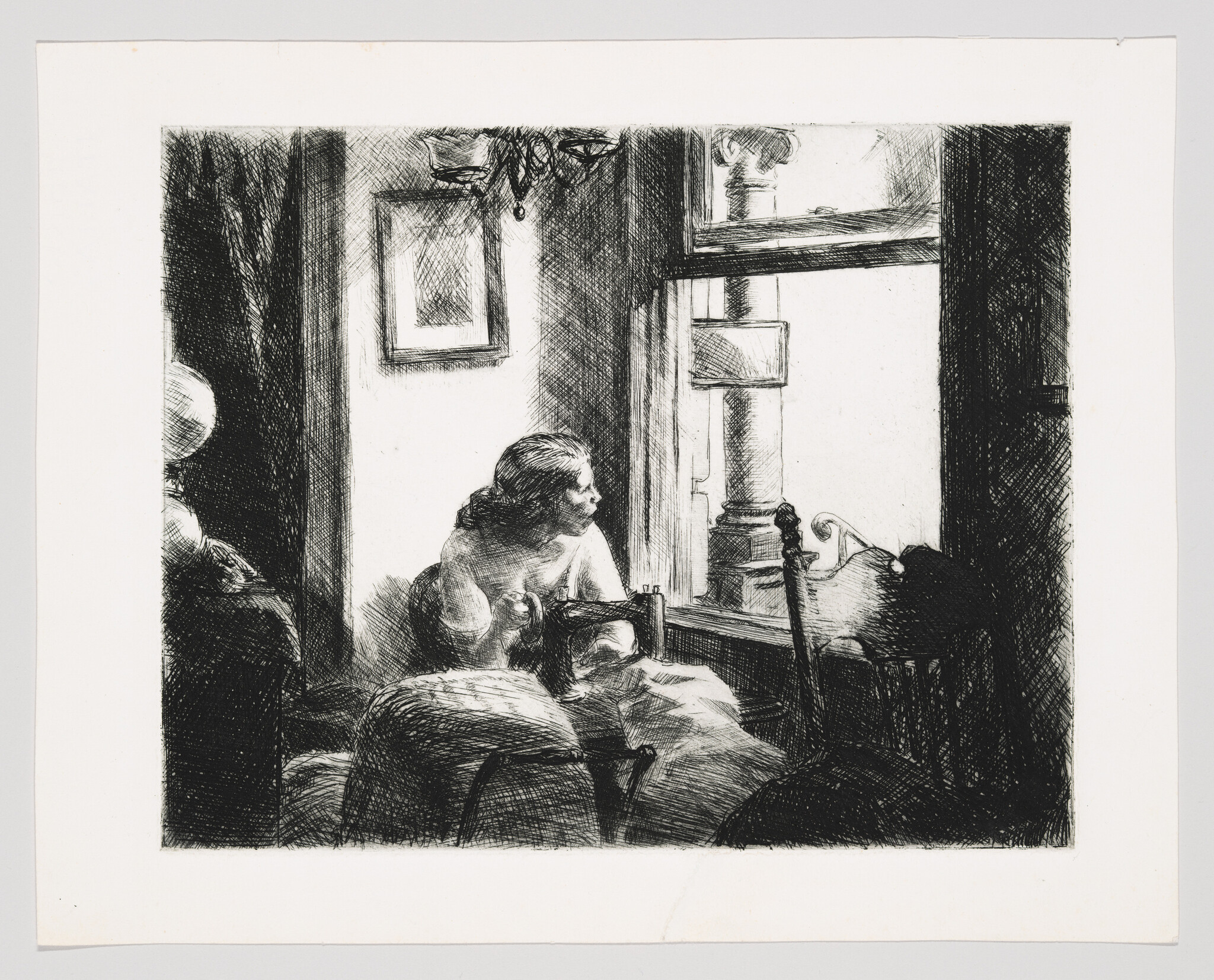 A woman sits by a window sewing and looks thoughtfully outside.