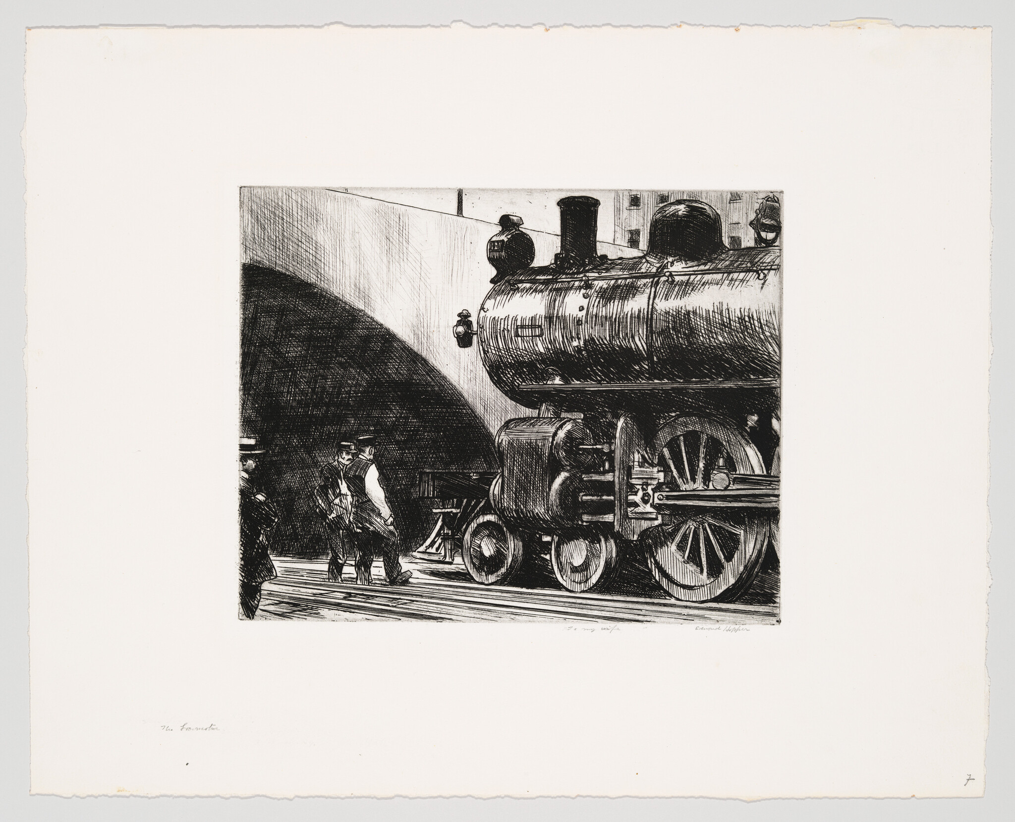 A large steam locomotive sits by a tunnel while two men walk beside it.