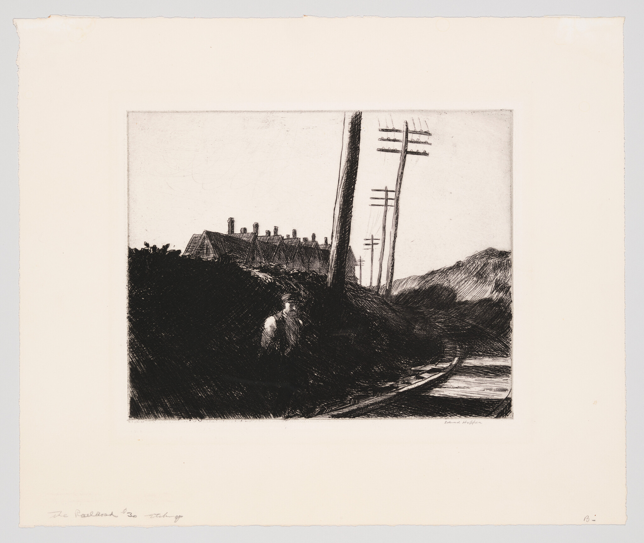 A lone man stands by a dark embankment near railroad tracks and leaning telegraph poles.
