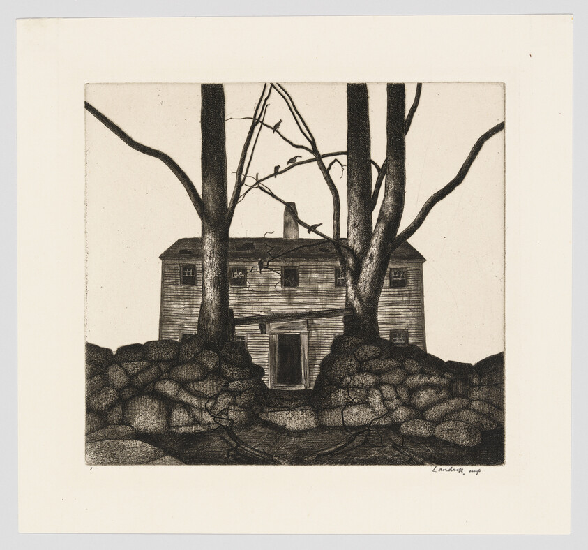 Old two-story wooden house stands behind large bare trees and a low stone wall.