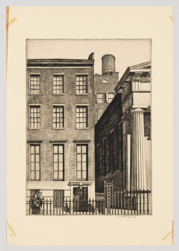 Row of brick buildings and classical-columned structure beside an iron fence with two people talking.