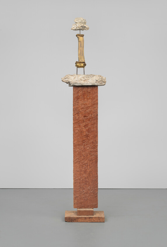 Tall wooden pillar topped with a rough stone slab and a small vertical gold sculpture.