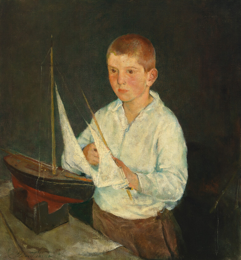 A young boy in a white shirt carefully adjusts the sails of a wooden model boat.